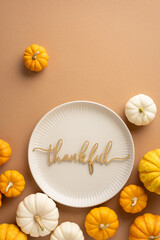 Top vertical view of Thanksgiving table setting with small pumpkins and a plate featuring the word thankful, conveying autumn gratitude and celebration