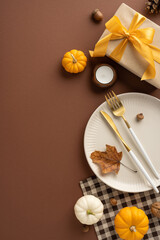 Elegant vertical Thanksgiving table arrangement featuring small pumpkins, a wrapped gift, and a stylish plate setting on a brown background