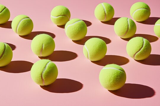 Row of tennis balls are lined up on a yellow surface. There are 14 balls in total. a uniform grid of neon green tennis balls on a clay coloured background