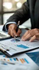 Business professional analyzing financial data and charts on a desk with documents, pen, and laptop in an office setting.
