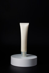 Plastic white tube for cream or lotion. Skin care or sunscreen cosmetic with stylish props on black background.