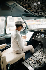 Asian Confident male pilot in uniform leaning at the passenger seat while standing inside of the airplane flight cockpit during takeoff and checking © Nuttapong punna