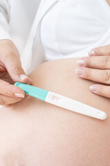 Pregnancy test in female hand on blurred female body wearing white underwear background.