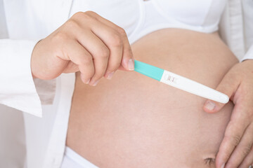 Pregnancy test in female hand on blurred female body wearing white underwear background.