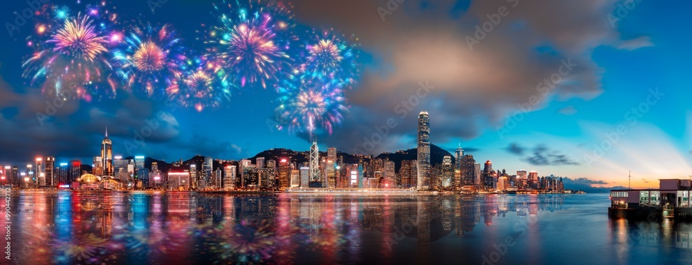 Poster fireworks explode over a vibrant hong kong cityscape, reflecting in the calm water.
