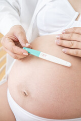 Pregnancy test in female hand on blurred female body wearing white underwear background.