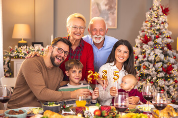 Happy family holding balloons shaped as numbers 2025 while having Christmas dinner
