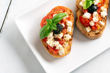Vassoio di deliziose bruschette con pomodoro fresco, mozzarella, olive, basilico e olio extravergine di oliva, spuntino italiano, dieta mediterranea 