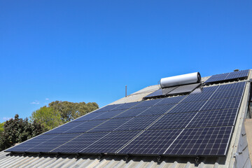 Solar panels, cells, array or photovoltaic (PV) electric modules, as well as hot water system on roof of house. Almost cloudless sky, Australia © BJP7images