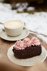 Aestetics vegan brownie witn no sugar cake dessert and cup of cappuccino outdoor at the snowy day. Coffee with dessert winter aesthetics.