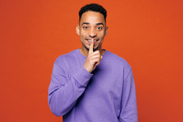 Young happy man of African American ethnicity wear purple sweatshirt casual clothes say hush be quiet with finger on lips shhh gesture isolated on plain red orange background studio Lifestyle concept