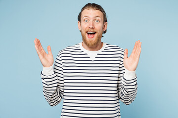 Naklejka premium Young shocked surprised overjoyed happy man he wear striped sweatshirt casual clothes look camera spread hands isolated on plain pastel light blue cyan background studio portrait. Lifestyle concept.