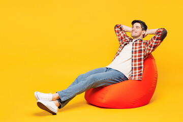 Full body young minded happy man he wears red checkered shirt casual clothes sit in bag chair hold...