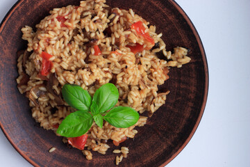 A plate of risotto, made with brown rice and cooked with vegetables and herbs. Garnished with a sprig of basil.
