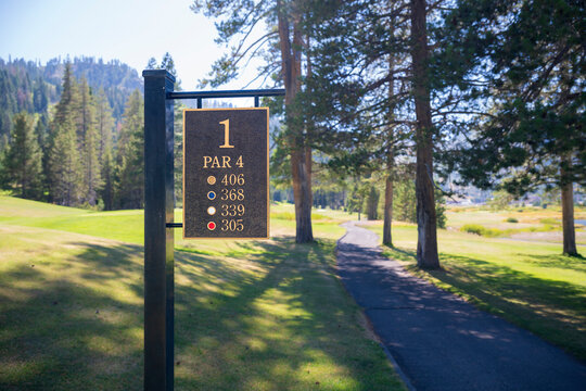 A signpost, indicating the forst hole on a golf course located in a beautiful pine valley, in California.  The sign states the length of the hole from various tees and that it is a par 4