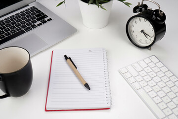 notebook with pen, alarm clock, laptop, keyboard, mug and plant on white background