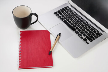 red notebook with pen, mug and laptop on white background