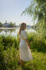 beautiful young artist in a white dress among the trees on the river bank