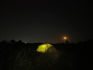 Illuminated tent under night starry sky with moon