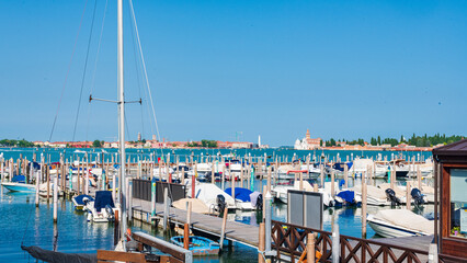 Petit port avec des bateaux à quai devant le quartier du Cannaregio à Venise dans la lagune avec la mer et un phare à l'arrière plan par une journée ensoleillée et un ciel bleu