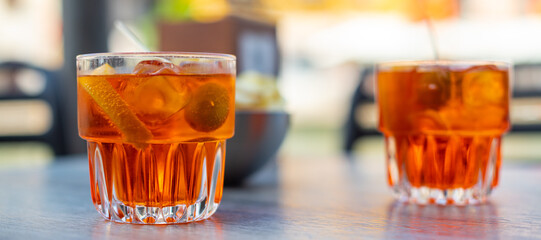 Deux verres de cocktail apéritif orange avec une olive et une pique à l'intérieur, posés sur une table de bar en extérieur et des chips à l'arrière plan par une fin de journée ensoleillée à Venise