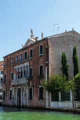Maison traditionnelle rouge à Venise vue du grand canal avec un quai et un ciel bleu à l'arrière plan par une journée ensoleillée.