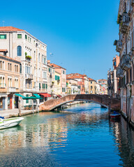 Vue d'un canal à Venise avec un pont en pierre et un quai avec des maisons traditionnelles en pierre et un ciel bleu à l'arrière-plan