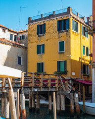 Maison jaune traditionnelle à Venise avec un ponton en bois donnant sur un canal avec un ciel bleu