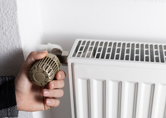 A man´s hand on a radiator temperature controller. heating system in european countries. seasonal...