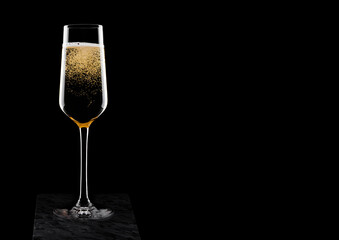 Elegant glass of yellow champagne with bubbles on black marble board on black background. Space for text