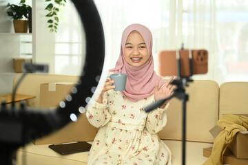 Young Muslim woman showing pottery products in front of smartphone camera while live streaming at home