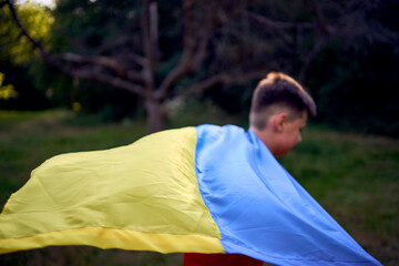 a preteen boy runs in the park with the flag of Ukraine