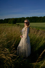 portrait of a young blonde woman in a pastel chiffon dress in a field of golden grass