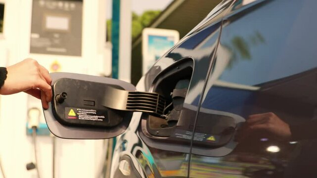 Young woman driving an EV electric car is parked in front charging station opening the side cover charge the electric car : Clean energy vehicle Alternative energy is becoming popular concept.