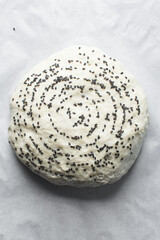 Overhead view of sourdough bread dough with black sesame seeds about to be baked, scored artisan bread dough on parchment lined baking tray, process of making homemade bread