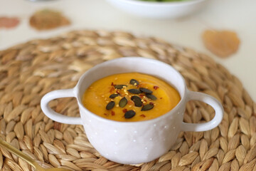 Pumpkin and potato creamy soup, bowl of grapes, jars of nuts and autumn leaves on the table. Selective focus.