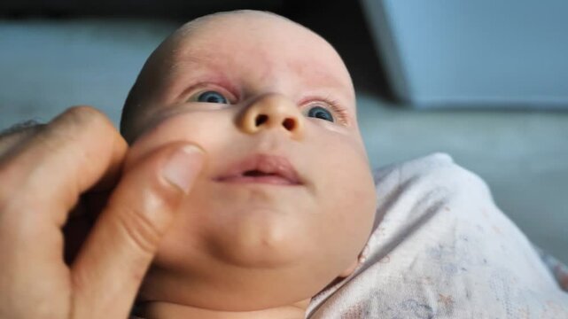 The parent's fingers gently pinch the infant's chubby cheek. A father pinches and pulls his newborn son's cheek. Parental love and care