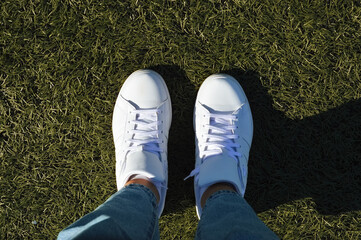 women's legs in jeans and new white leather sneakers on the artificial turf of a football field....