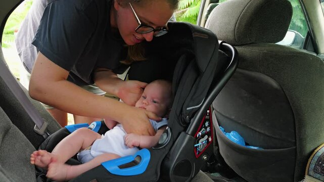 The woman places the infant in the car seat and fastens the seat belts to ensure the safety of the child during the journey