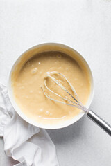 Overhead view of vanilla cake batter being whisked in a white ceramic bowl, flatlay of cake batter being mixed, process of making cake