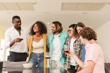 Joyful multi-racial friends having a conversation and laughing together at a dining table, smiling as they enjoy champagne in a warm and loving toast, sharing a moment of togetherness and celebration.