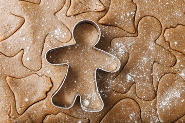 Cooking ginger cookies, Christmas and New Year traditional cookies in shape of gingerbread man, raw rolled out dough with cut out dough figures, closeup texture, top view, metal pastry cutter on dough