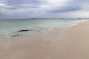 A minimalist view of Gurteen Beach in Ireland, highlighting the soft pastel colors of the sand and sea at sunset. The gentle diagonal of the shoreline leads into the turquoise waters of the Atlantic