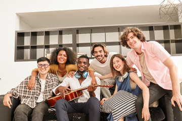 A group of multiracial teenagers playing guitar and singing a song together at an afternoon party. A group of Millennials sitting and spending time together on the holiday weekend..