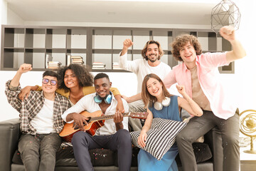 A group of multiracial teenagers playing guitar and singing a song together at the afternoon party. A group of Millennials sitting and raising their hands to celebrate the holiday weekend together.