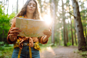 Naklejka premium A traveler woman stands in a lush forest, examining a map with a focused expression. Enjoying a beautiful day outdoors