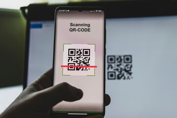 businessman sitting at his workplace in front of computer monitor and scanning QR code with mobile smart phone.