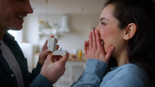 Caucasian male man husband boyfriend guy make proposal marry me propose give gift wedding ring at home to amazed shocked happy woman girl female wife girlfriend agree love couple date family affection