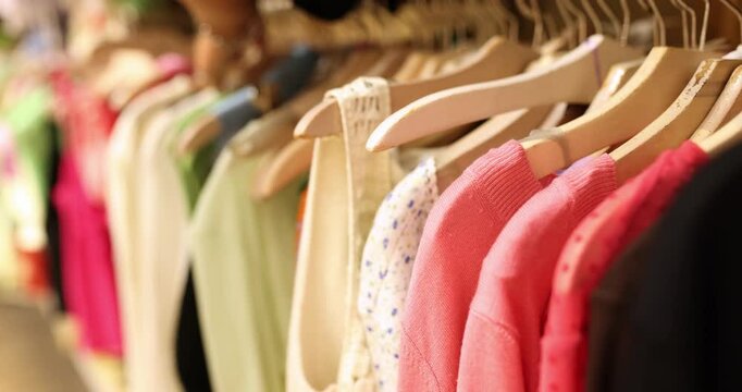 Many bright women's things hang on hangers, close-up, shallow focus. Second hand shop, clothes warehouse