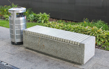 A concrete bench is next to a shiny stainless steel trash can